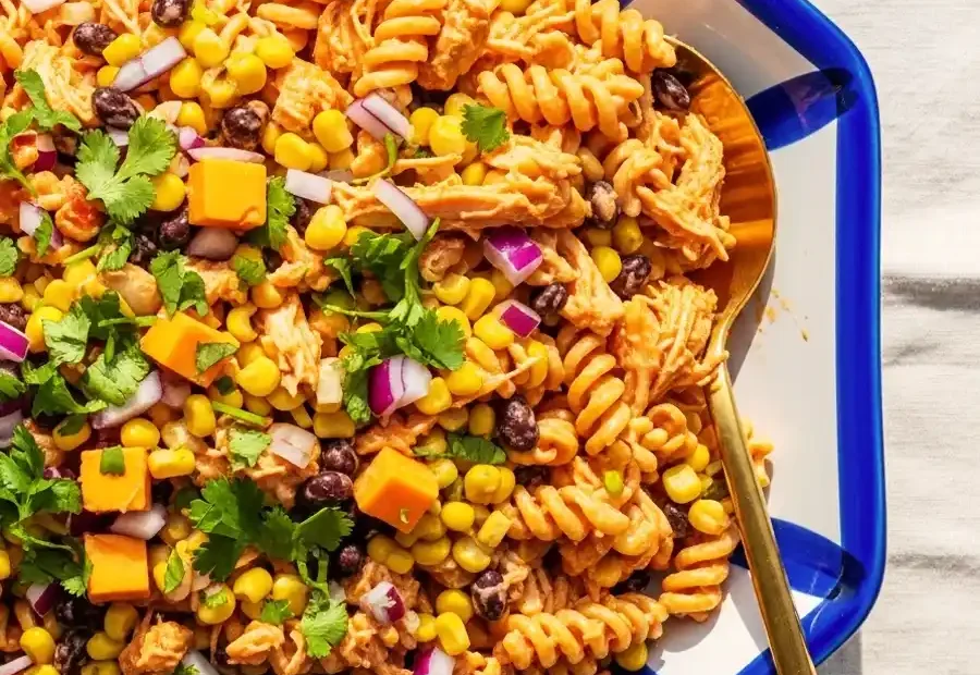 An overhead shot of a Southwestern BBQ chicken pasta salad in a decorative serving dish, featuring rotini pasta, shredded chicken, black beans, corn, diced cheddar cheese, and red onion, garnished with fresh cilantro.