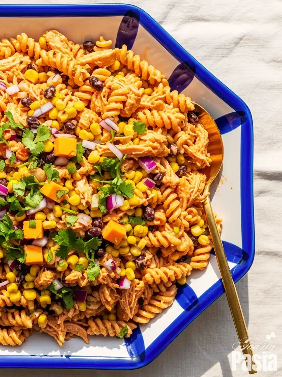 An overhead shot of a Southwestern BBQ chicken pasta salad in a decorative serving dish, featuring rotini pasta, shredded chicken, black beans, corn, diced cheddar cheese, and red onion, garnished with fresh cilantro.