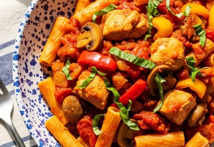 A rustic blue-speckled bowl of Chicken Cacciatore pasta, featuring rigatoni tossed with sautéed chicken, mushrooms, and bell peppers in a chunky, hunter-style tomato sauce, garnished with fresh basil.