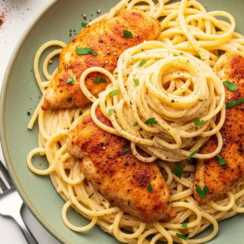 A green plate of creamy chicken gorgonzola pasta, featuring spaghetti in a rich blue cheese cream sauce, topped with paprika-seasoned pan-seared chicken and fresh parsley.