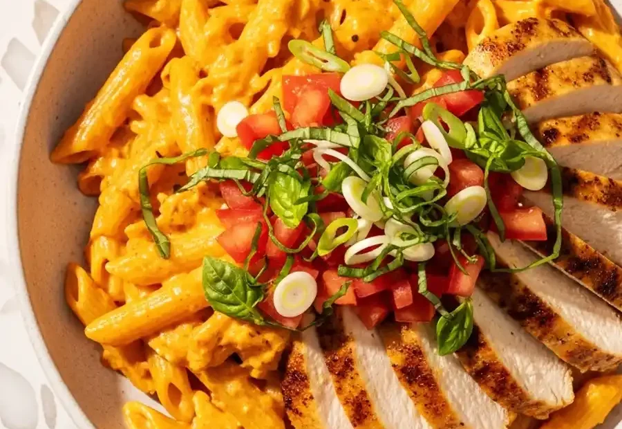 A bowl of copycat Firebirds Chicken Pasta, with penne in a spicy Asiago cream sauce, topped with sliced grilled chicken, and a fresh garnish of diced tomatoes, basil, and green onions.
