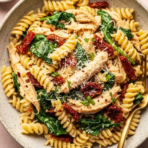 A close-up view of Marry Me Chicken Pasta, featuring rotini pasta with shredded chicken, sun-dried tomatoes, and fresh spinach in a creamy garlic-parmesan sauce, topped with red pepper flakes.