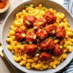 A bowl of Nashville Hot Chicken Mac and Cheese, featuring creamy elbow macaroni topped with crispy, spicy fried chicken bites tossed in a cayenne-based hot sauce and garnished with green onions.
