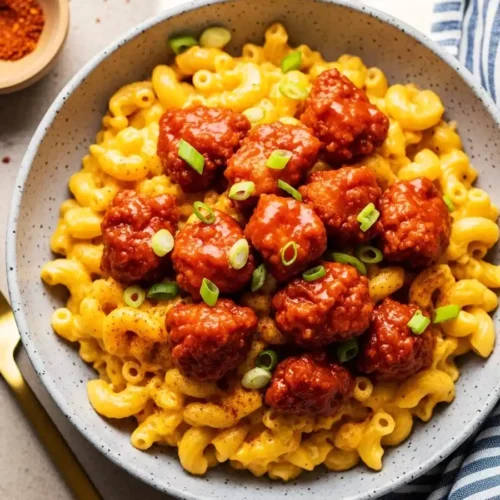A bowl of Nashville Hot Chicken Mac and Cheese, featuring creamy elbow macaroni topped with crispy, spicy fried chicken bites tossed in a cayenne-based hot sauce and garnished with green onions.
