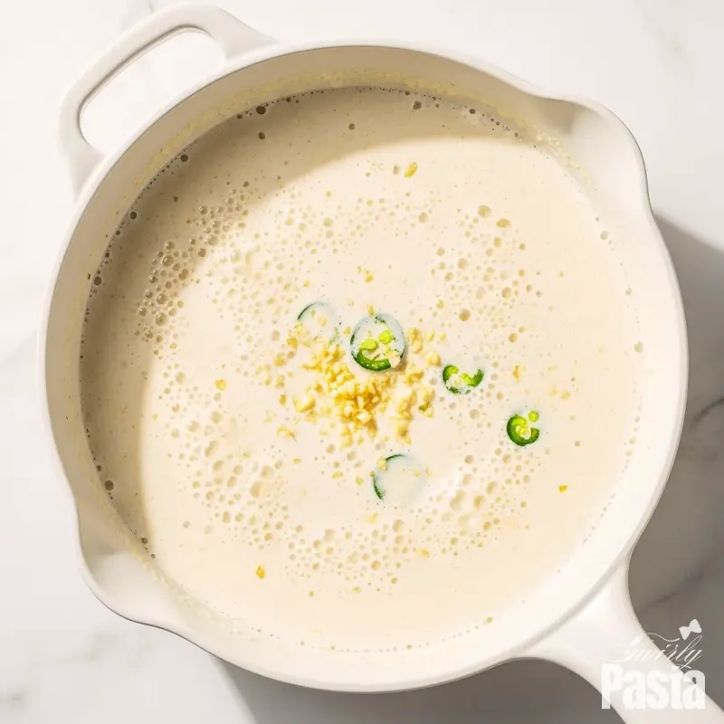 A flat lay view of a creamy white sauce simmering gently in a white pan.